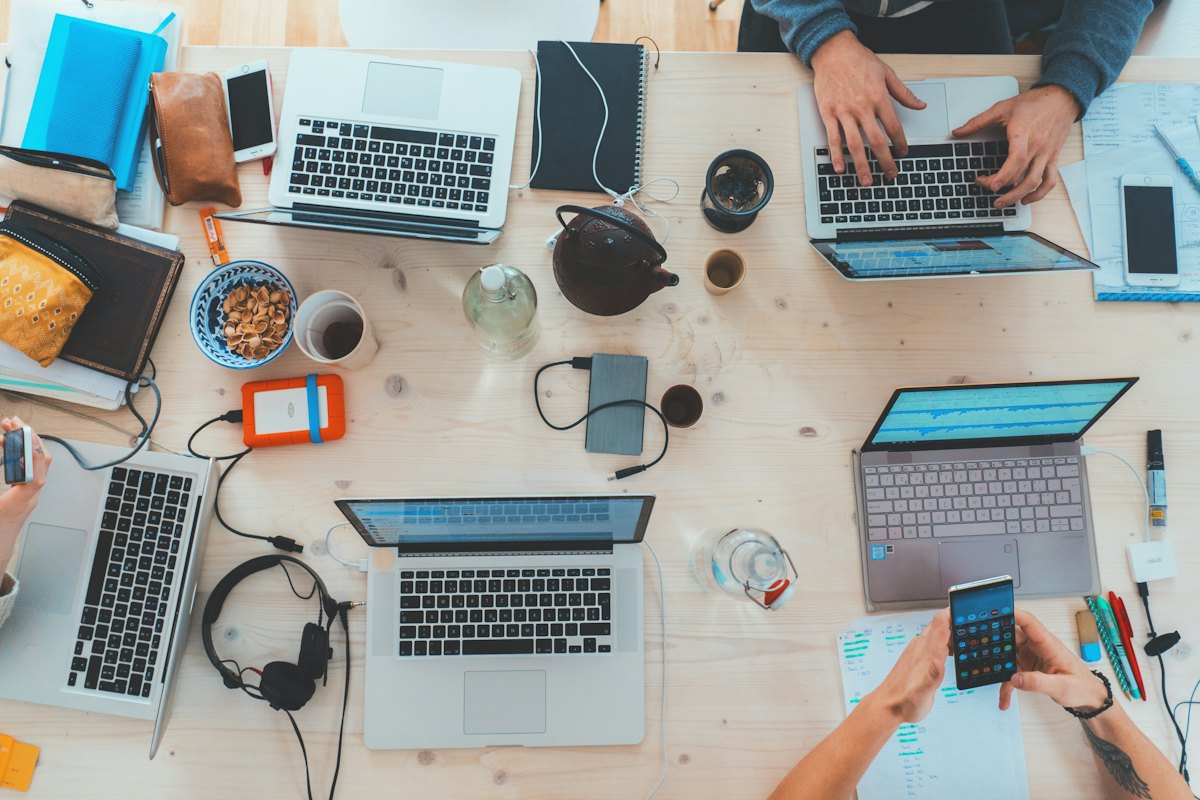 Vue du dessus d'une table de travail avec ordinateurs, carnets et mains d'une équipe